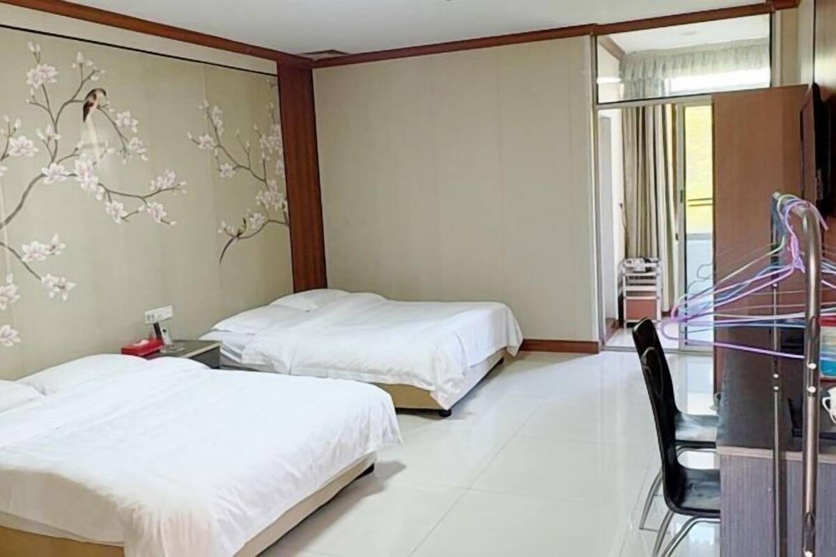 A hotel room with two beds, a wooden-framed TV, and a view of the outside balcony.