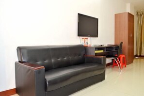 A black leather sofa with wooden armrests, a flat-screen TV mounted on the wall, a wooden cabinet, and a red stool. - Shengtai Hotel (Boluo)