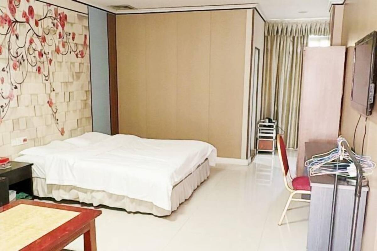 A hotel room with a bed, a desk, a chair, a TV, and a wardrobe.