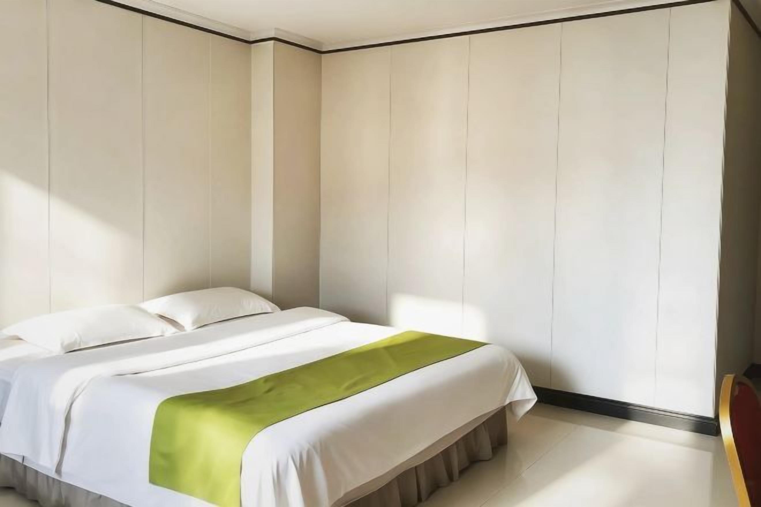 Un dormitorio con cama, un plaid verde y paredes blancas.