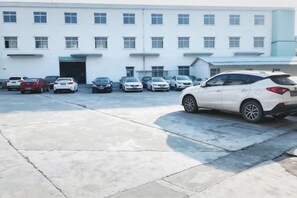 A parking lot with several cars, a white building with multiple windows and a door, and a clear sky. - Shengtai Hotel (Boluo)