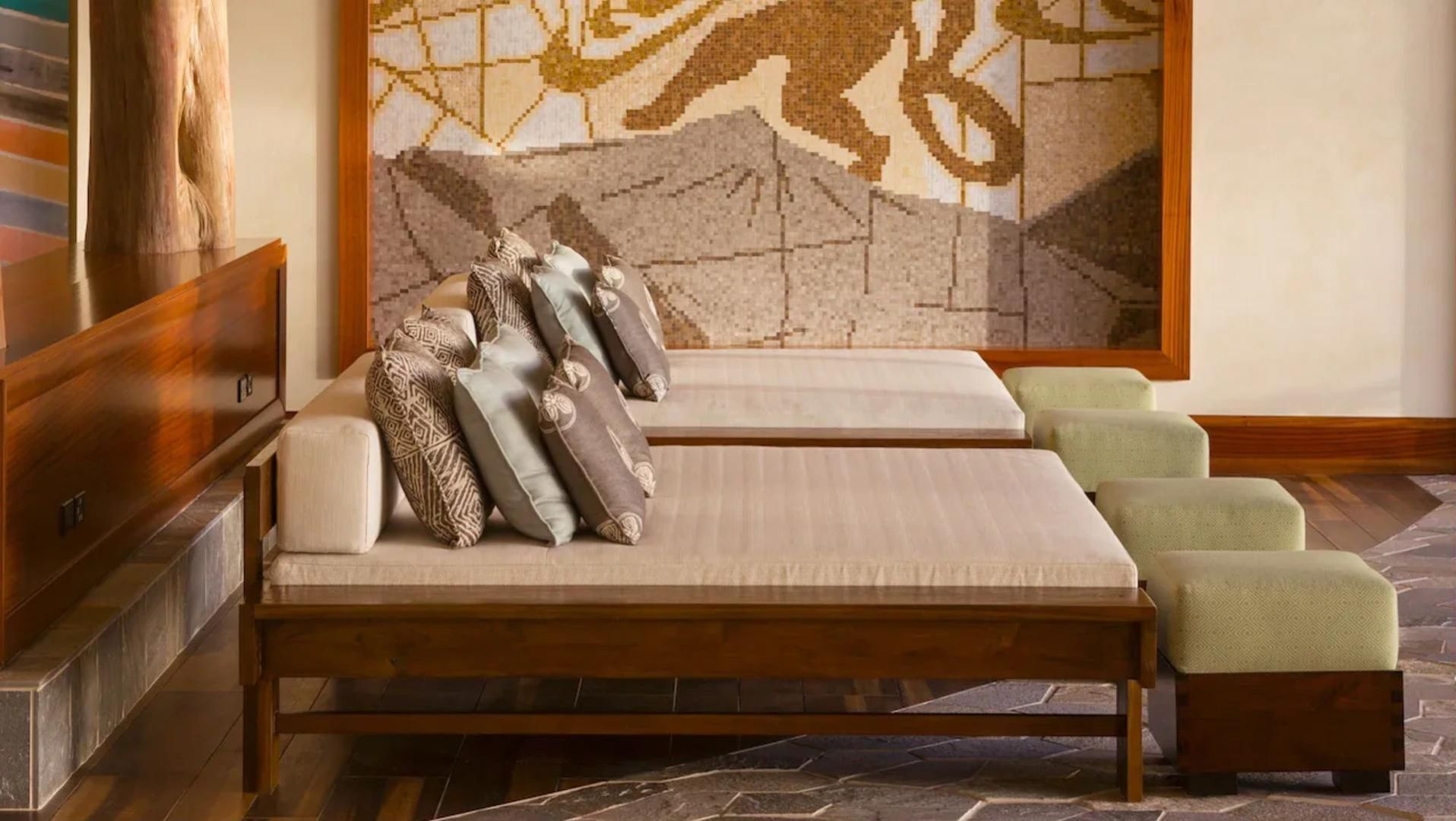 A spa room with a wooden bench, multiple pillows, and a stone floor.