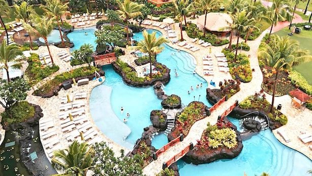 Un resort con varias piscinas, palmeras y zonas de descanso.