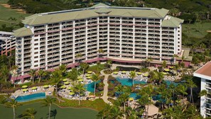 Un gran hotel con múltiples balcones, una piscina central y un área de piscina ajardinada con sillas de descanso y sombrillas.
