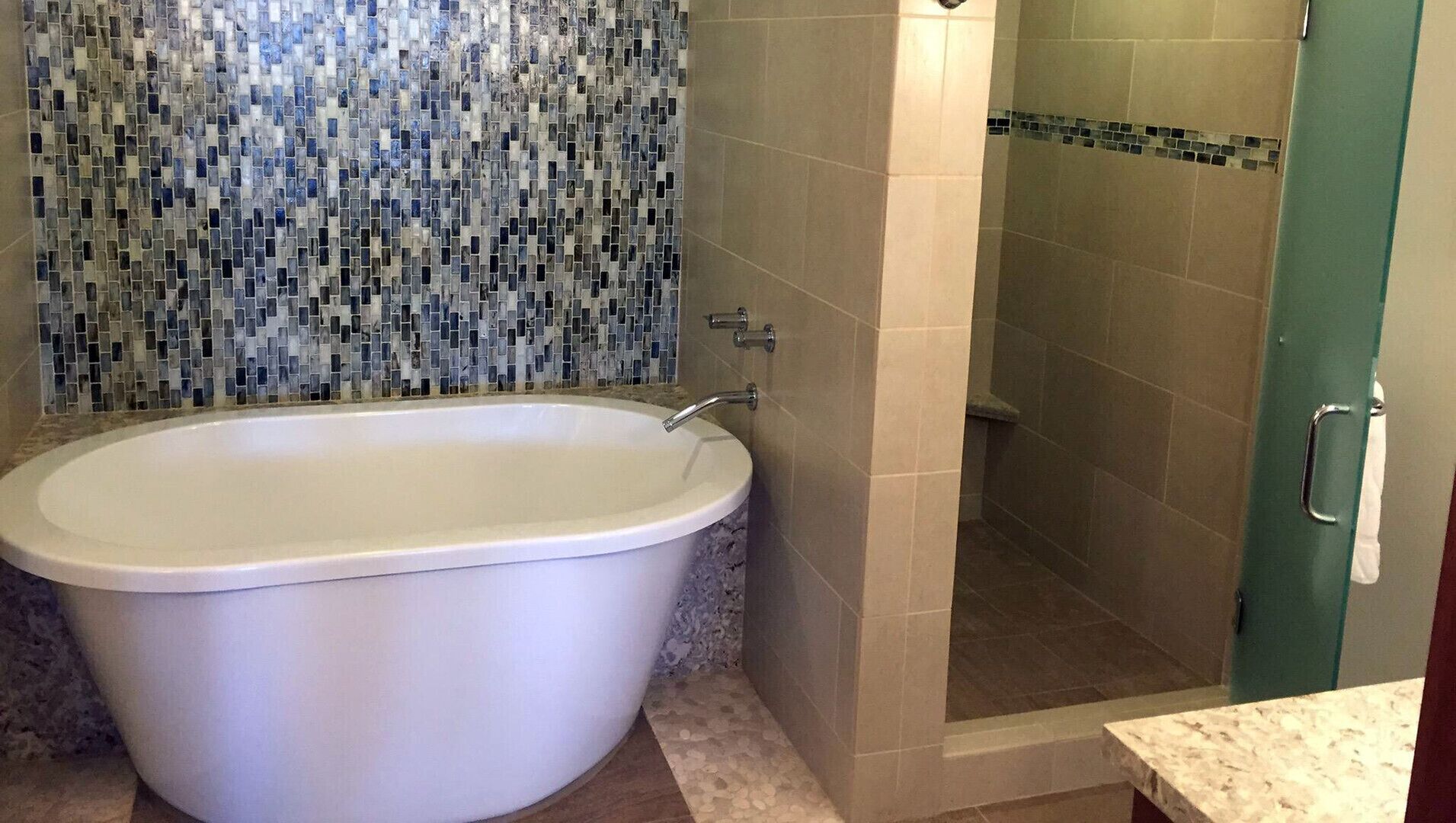 Un baño con una bañera independiente, ducha con puerta de cristal y pared de ducha azulejada.