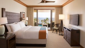 A hotel room with a large bed, a TV, a desk, and a balcony with a view of the ocean.