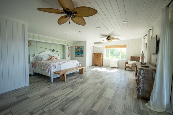 A spacious bedroom with a large bed, a bench, a dresser, and two ceiling fans.