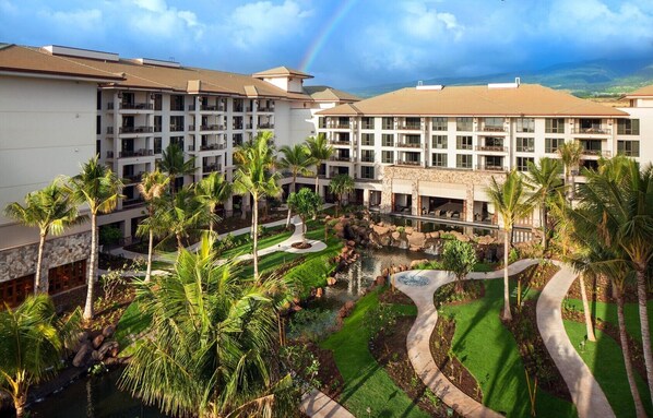 Ein Hotel mit mehreren Etagen, einem Innenhof mit Palmen, einem kleinen Wasserspiel und Blick auf die Landschaft.