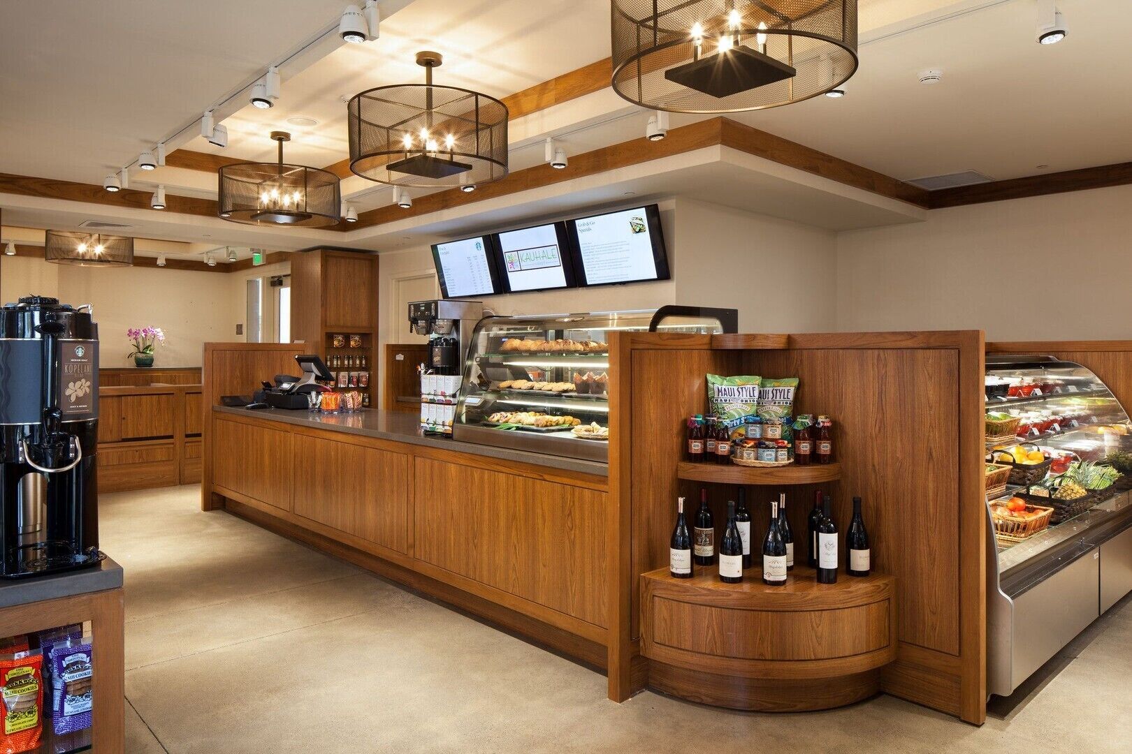 A coffee shop with a wooden counter, a coffee machine, a menu board, and a display case with snacks and drinks.
