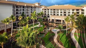 A hotel with multiple floors, a courtyard with palm trees, a small water feature, and a view of the landscape.