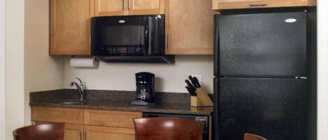 Una cocina compacta con armarios de madera, un microondas negro, un refrigerador negro, una cafetera y una mesa de comedor con sillas.