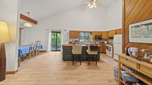 A spacious kitchen with wooden cabinets, a central island with bar stools, and a dining area with a blue tablecloth. - Spacious Home to Create Memories - access to Bay river and beaches (Millsboro)