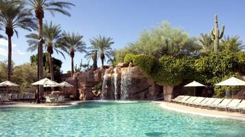 Ein Pool mit Wasserfall, umgeben von Palmen und Kakteen.