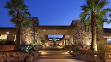 A hotel entrance with a stone facade, palm trees, and a staircase leading to the main building.