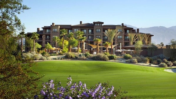 A multi-story hotel with a landscaped front lawn and palm trees.