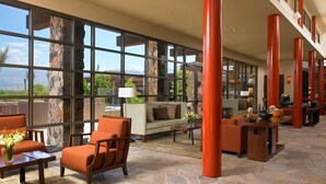 A spacious lobby with large windows, a stone fireplace, and a seating area with orange chairs and a sofa.