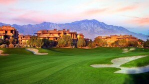 A golf course with multiple buildings in the background and mountains.