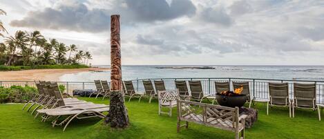 Un área de descanso en la playa con una fogata y sillones, con vista al océano.