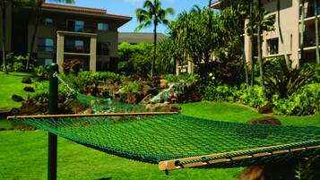 Un hamac dans un jardin luxuriant, avec une cascade, des palmiers et un bâtiment en arrière-plan.
