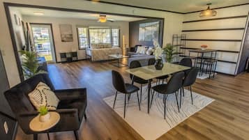 Un salon moderne comprenant un coin repas, un plancher en bois et une grande fenêtre laissant entrer la lumière naturelle.
