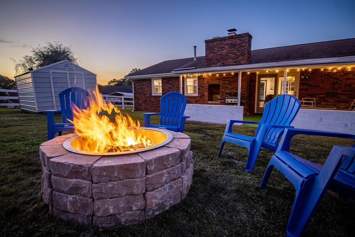 A backyard with a stone fire pit, blue chairs, and a house with a covered porch.