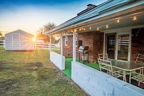 A covered patio with a barbecue grill, outdoor seating, and a shed in the background.