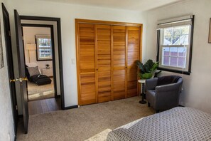 A bedroom with a large closet, a window with blinds, a chair, and a bed.