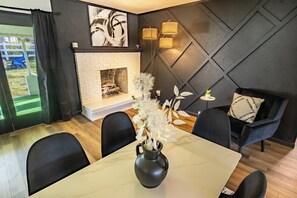 A modern living room with a fireplace, a dining table with chairs, and a sofa with a patterned pillow.