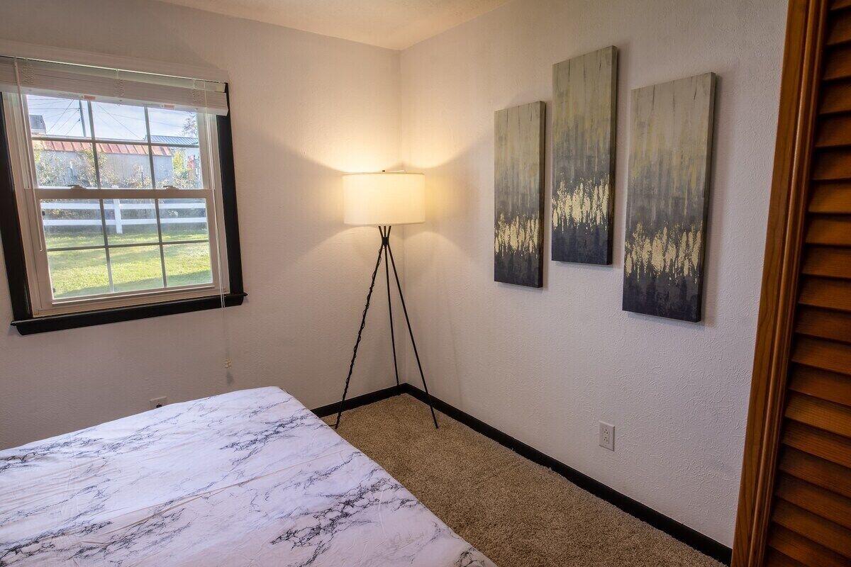 A bedroom with a bed, a floor lamp, and three wall-mounted paintings.