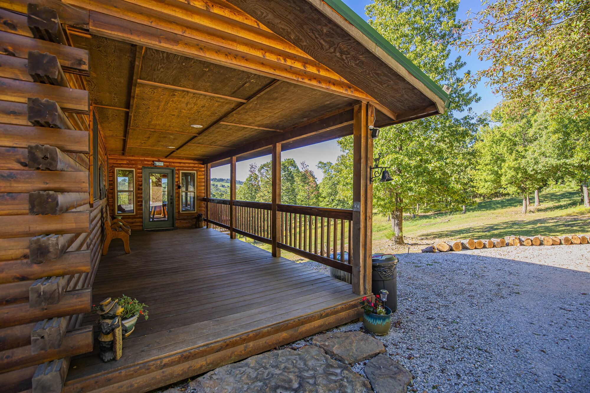 A log cabin with a wooden porch, a door leading inside, and a view of a green landscape.