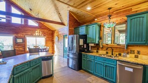 L’intérieur d’un chalet en bois comprend une cuisine avec des armoires de couleur turquoise, des appareils en acier inoxydable et un coin repas agrémenté d’un lustre.