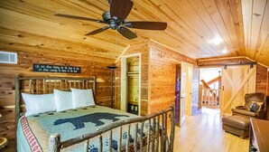 Une chambre dans une cabane en bois, avec un lit, un ventilateur de plafond et un panneau accroché au mur.