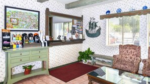 Um quarto com uma mesa consola verde, um tapete vermelho, uma mesa de centro com tampo de vidro, uma poltrona estampada e uma decoração de navio na parede.