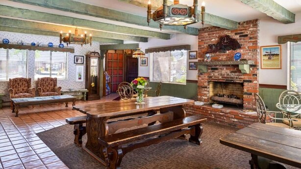Um interior rústico com uma grande mesa de madeira, bancos e uma lareira de tijolos.