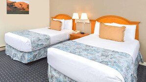 Quarto de hotel com duas camas de solteiro, uma mesa de cabeceira com abajur e um quadro na parede.