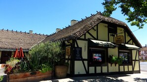 Um edifício tradicional em estilo de enxaimel com uma placa indicando café e vinho, rodeado por vasos de plantas.