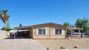 A single-story mobile home with a covered porch, a gravel driveway, and a palm tree in the background.