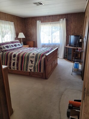 A bedroom with a wooden bed, a TV on a stand, a lamp, and a window with curtains. - Family home with everything you need (Phoenix)