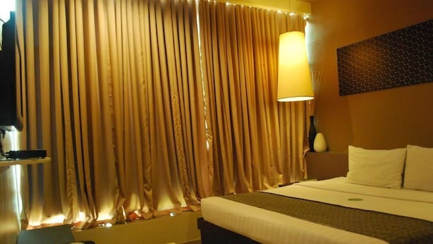 A hotel room with a bed, a desk, a lamp, and curtains.