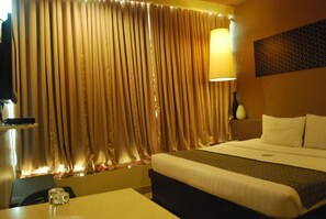 Una habitación de hotel con cama, escritorio, lámpara y cortinas.