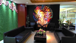 A lobby with black leather sofas, a central coffee table with a floral arrangement, and a large colorful mural on the wall.