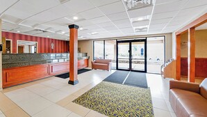 Un hall con mostrador de recepción, alfombra estampada, zona de estar y puerta de vidrio que da al exterior.