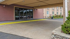 Entrada de un edificio con marquesina, puerta de cristal y zona de estacionamiento.
