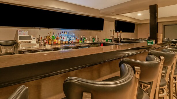 Zona de bar con una barra larga, varios taburetes y una amplia variedad de botellas.