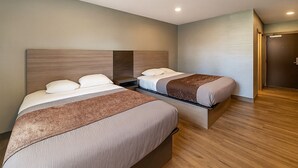Habitación de hotel con dos camas, piso de madera y una puerta a la derecha.