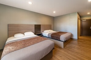 Hotellihuone, jossa on kaksi sänkyä, puulattia ja ovi oikealla puolella.