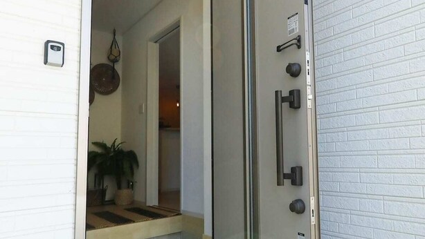A modern entrance with a glass door, a security camera above, and a small potted plant inside. - Condomium Motobu Sakura Terrace (Motobu)