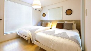 A bedroom with two beds, a ceiling light, and a wall-mounted air conditioner. - Condomium Motobu Sakura Terrace (Motobu)