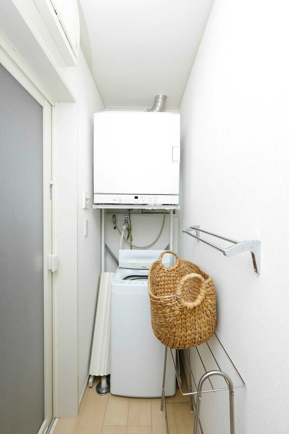 A compact laundry room with a white washing machine, a metal drying rack, and a woven basket.