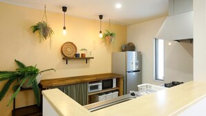 A modern kitchen with a wooden countertop, a built-in microwave, a stainless steel refrigerator, and hanging plants. - Condomium Motobu Sakura Terrace (Motobu)